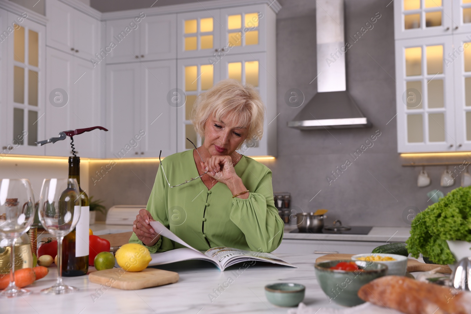 Senior woman with glasses reading magazine at marble table in kitchen Photo of Senior woman with glasses reading magazine at marble table in kitchen