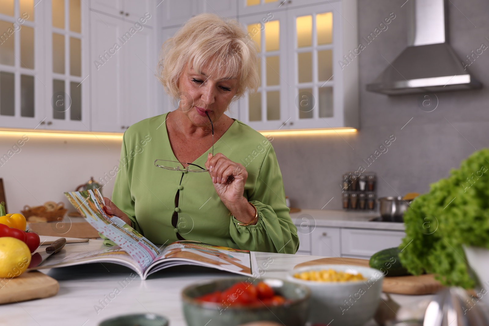 Senior woman with glasses reading magazine at marble table in kitchen Photo of Senior woman with glasses reading magazine at marble table in kitchen