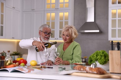 Photo of Elderly couple drinking white wine while cooking at table in kitchen
