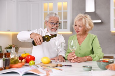 Photo of Elderly couple drinking white wine while cooking at table in kitchen