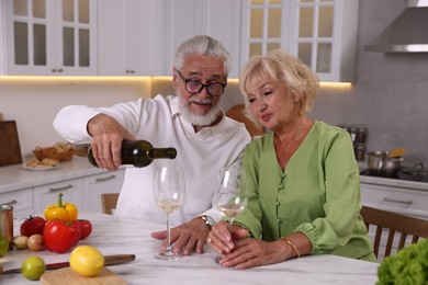Photo of Elderly couple drinking white wine while cooking at table in kitchen