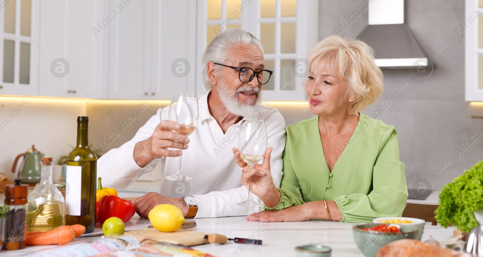 Elderly couple drinking white wine while cooking at table in kitchen Photo of Elderly couple drinking white wine while cooking at table in kitchen