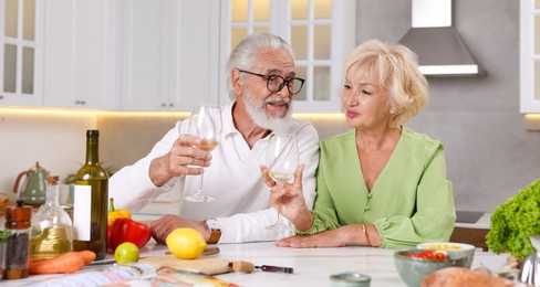 Photo of Elderly couple drinking white wine while cooking at table in kitchen