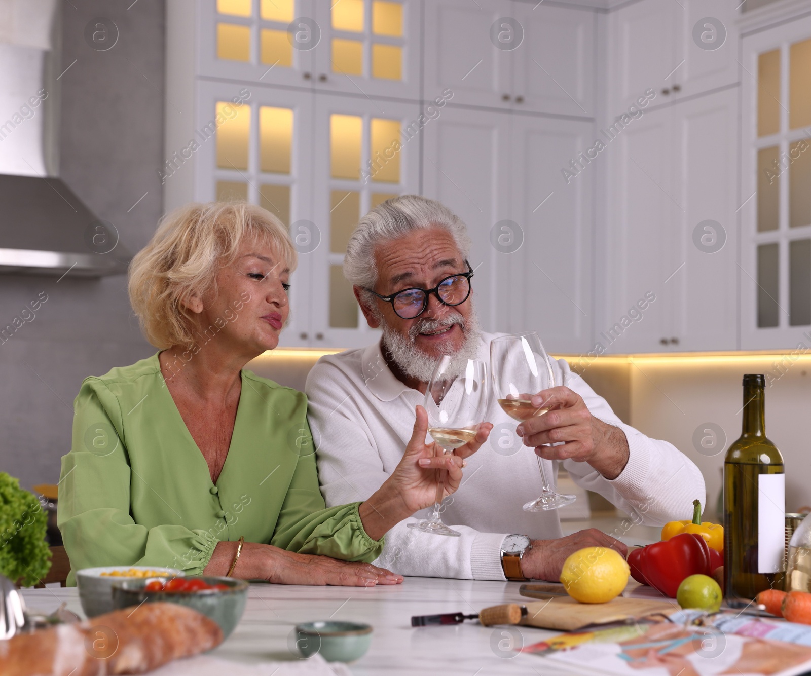 Elderly couple drinking white wine while cooking at table in kitchen Photo of Elderly couple drinking white wine while cooking at table in kitchen