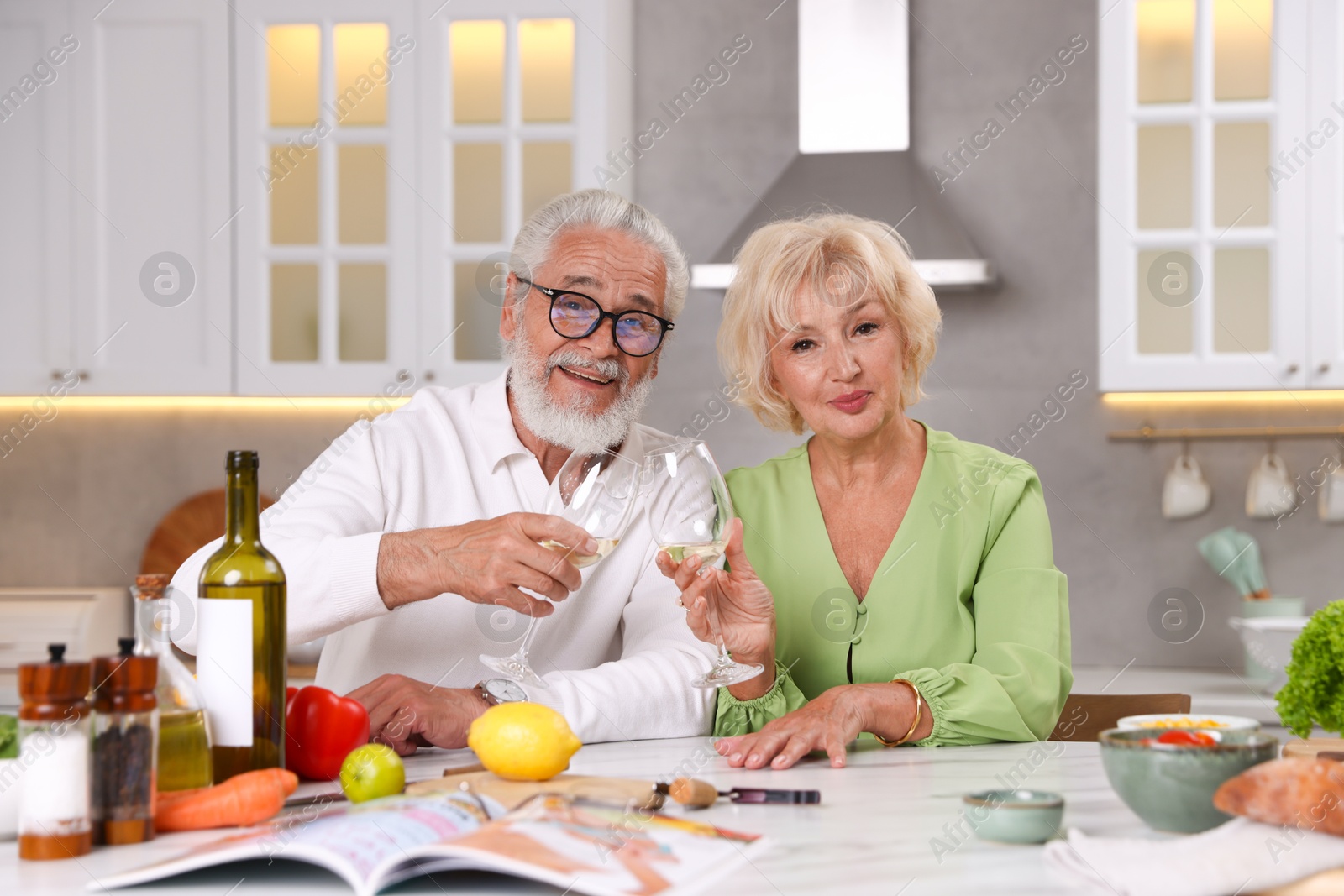 Elderly couple drinking white wine while cooking at table in kitchen Photo of Elderly couple drinking white wine while cooking at table in kitchen