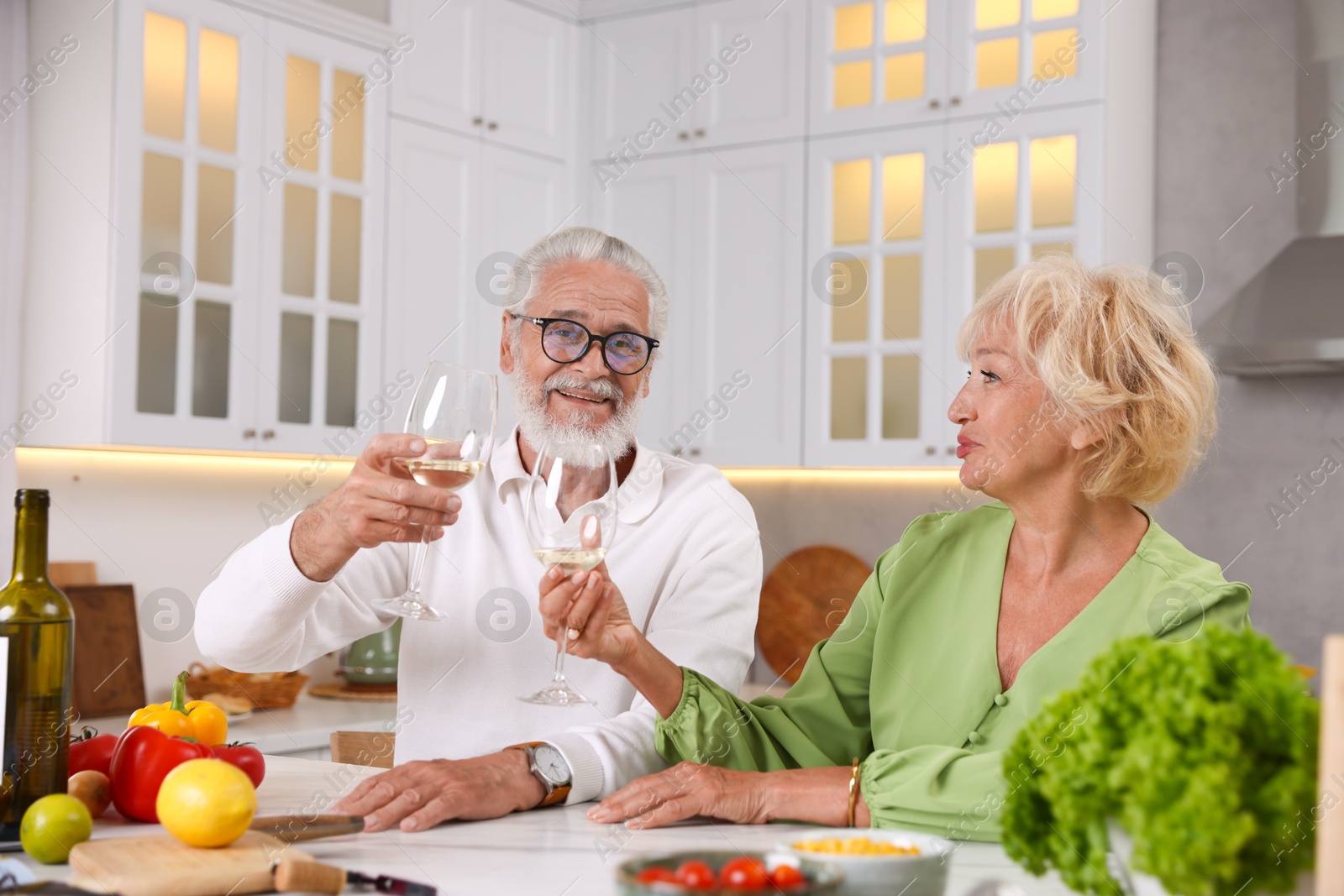 Elderly couple drinking white wine while cooking at table in kitchen Photo of Elderly couple drinking white wine while cooking at table in kitchen