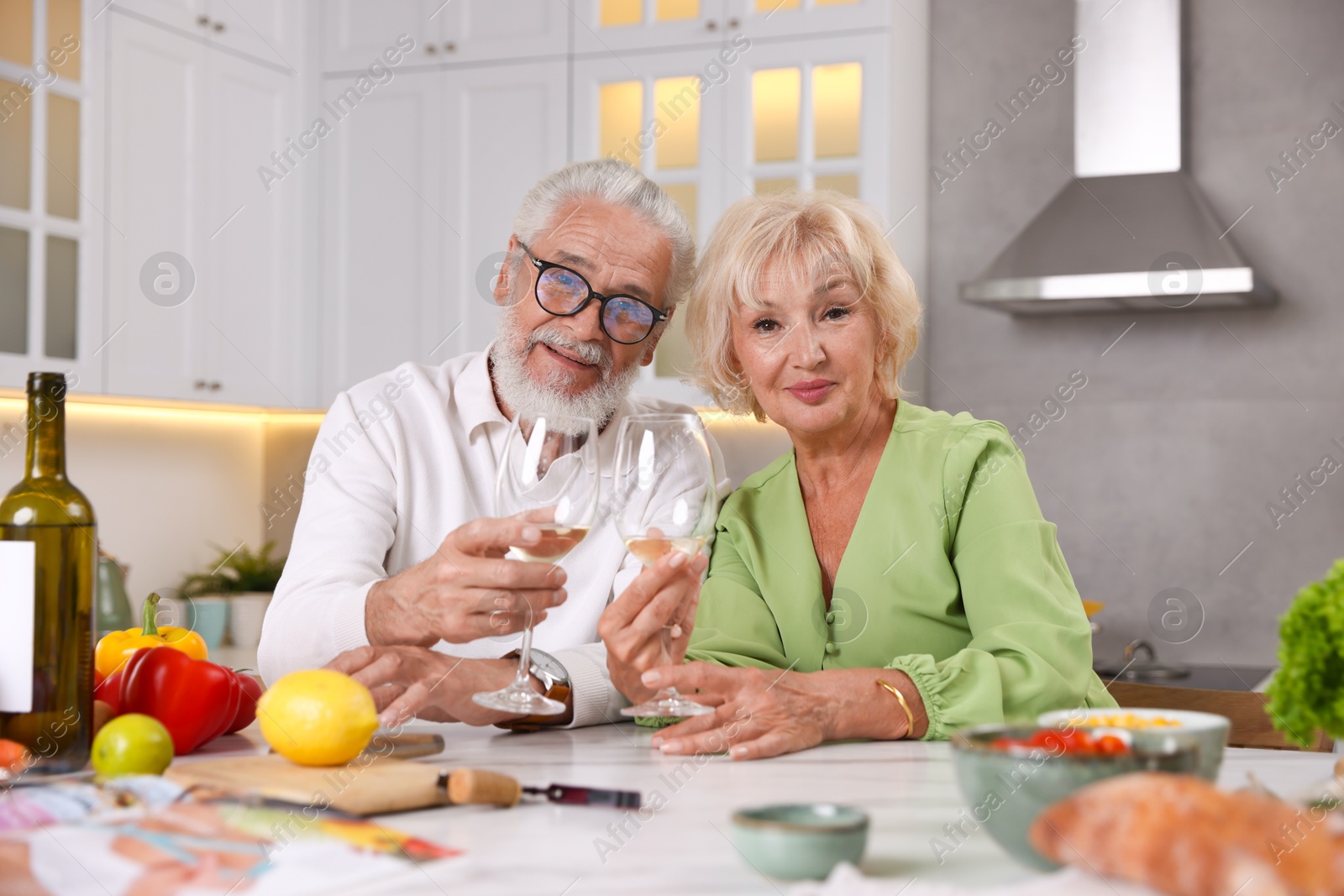 Elderly couple drinking white wine while cooking at table in kitchen Photo of Elderly couple drinking white wine while cooking at table in kitchen