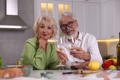 Photo of Elderly couple drinking white wine while cooking at table in kitchen