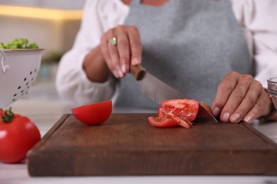 Photo of Senior woman cutting tomato at table in kitchen, closeup