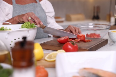 Photo of Senior woman cutting tomato at table in kitchen, closeup