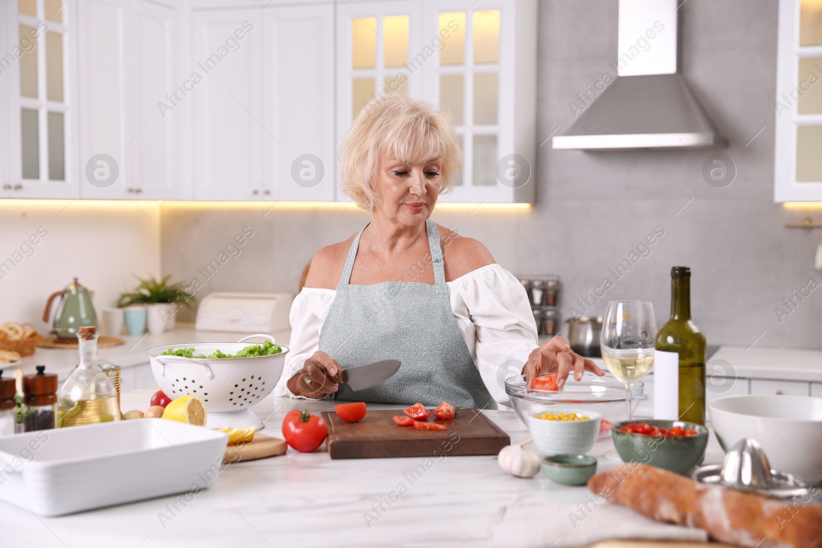 Senior woman cooking at table in kitchen Photo of Senior woman cooking at table in kitchen