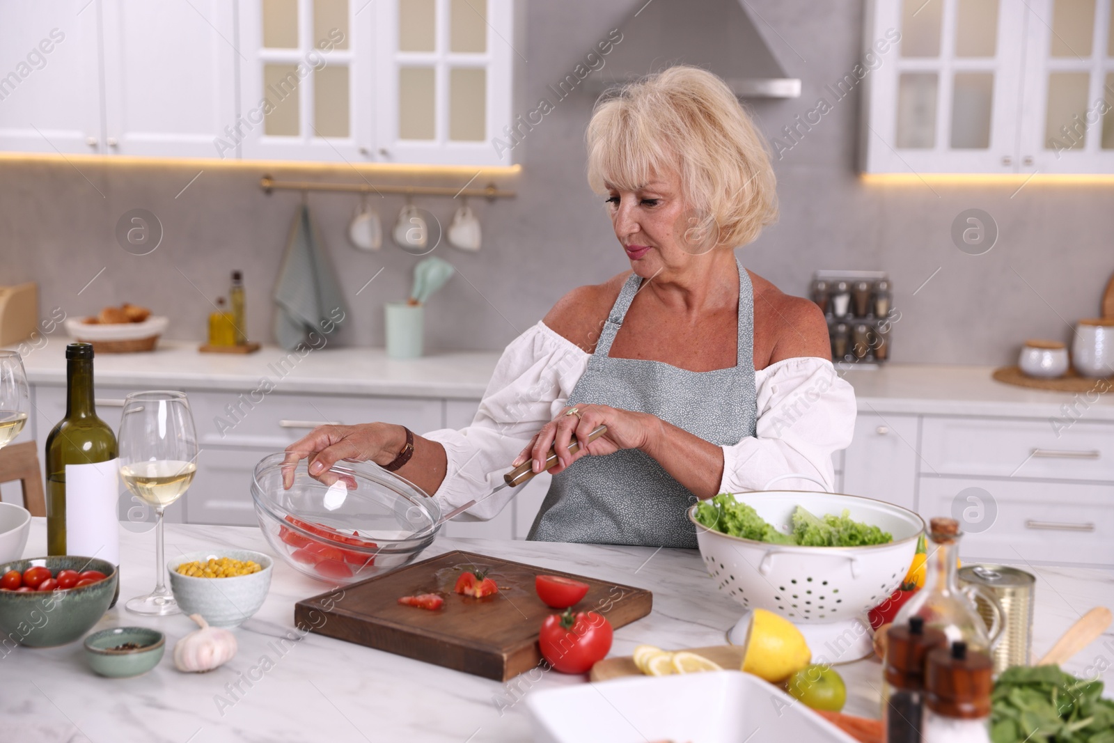 Senior woman cooking at table in kitchen Photo of Senior woman cooking at table in kitchen
