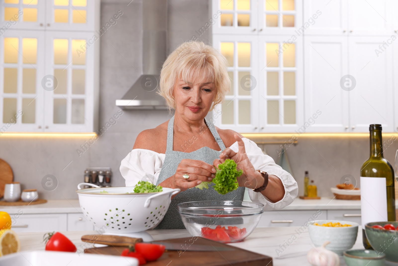 Senior woman cooking at table in kitchen Photo of Senior woman cooking at table in kitchen