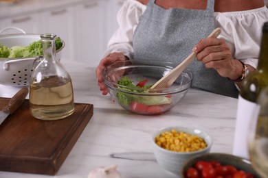 Photo of Senior woman cooking at marble table indoors, closeup