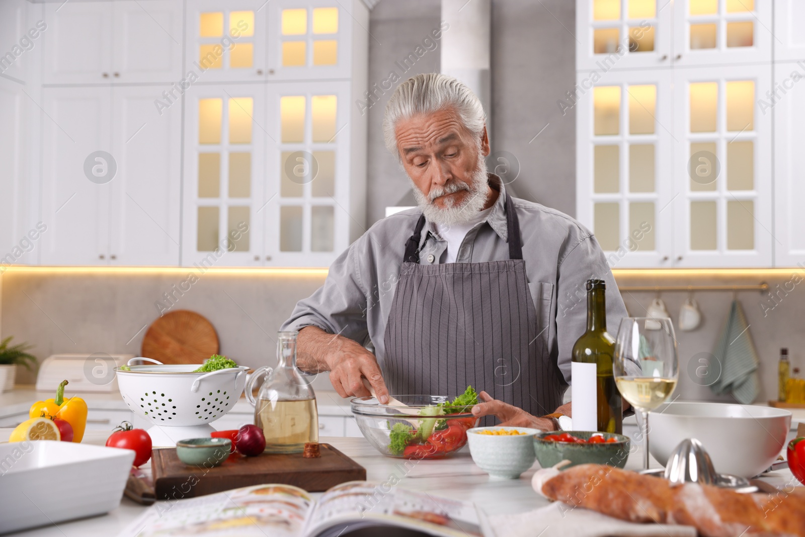 Elderly man cooking at table in kitchen Photo of Elderly man cooking at table in kitchen