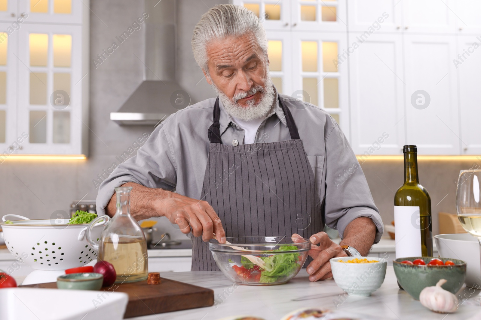 Elderly man cooking at table in kitchen Photo of Elderly man cooking at table in kitchen