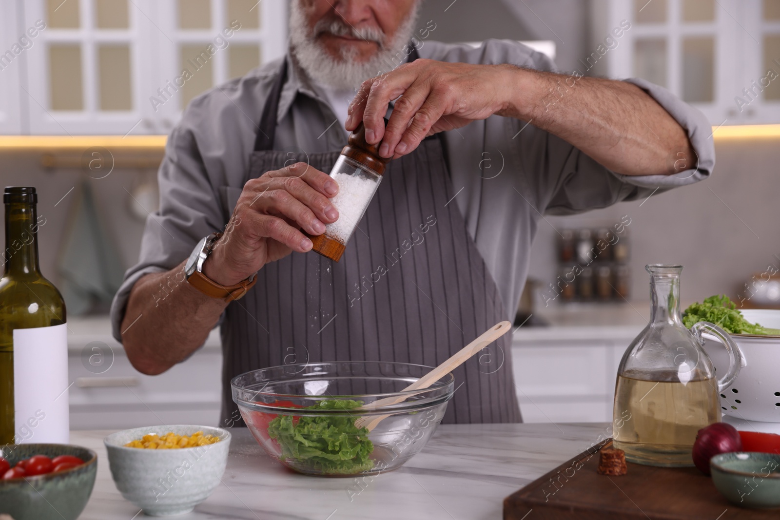 Elderly man salting salad at marble table in kitchen, closeup Photo of Elderly man salting salad at marble table in kitchen, closeup