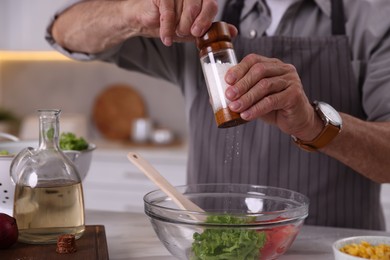 Photo of Elderly man salting salad at marble table in kitchen, closeup