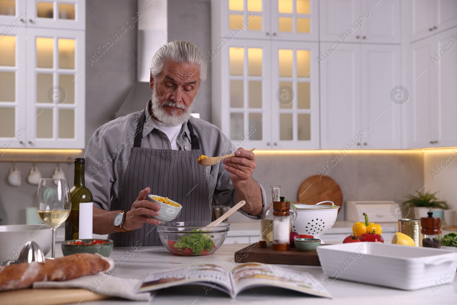 Elderly man cooking at table in kitchen Photo of Elderly man cooking at table in kitchen