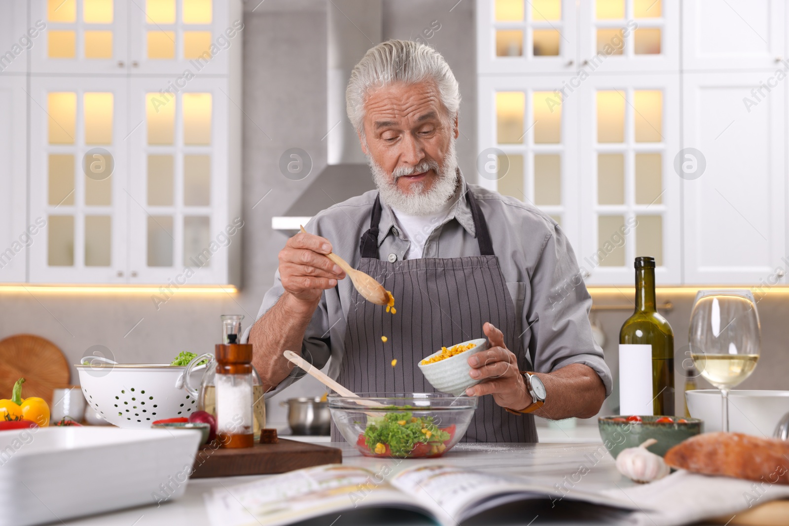 Elderly man cooking at table in kitchen Photo of Elderly man cooking at table in kitchen