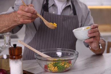 Photo of Elderly man cooking at marble table indoors, closeup