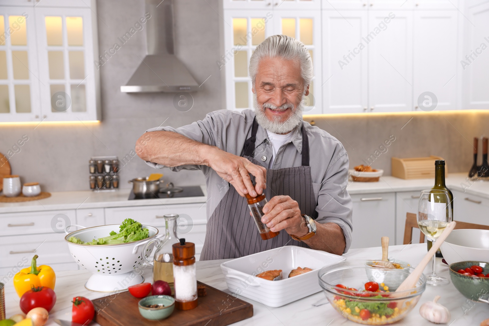 Smiling elderly man cooking at table in kitchen Photo of Smiling elderly man cooking at table in kitchen