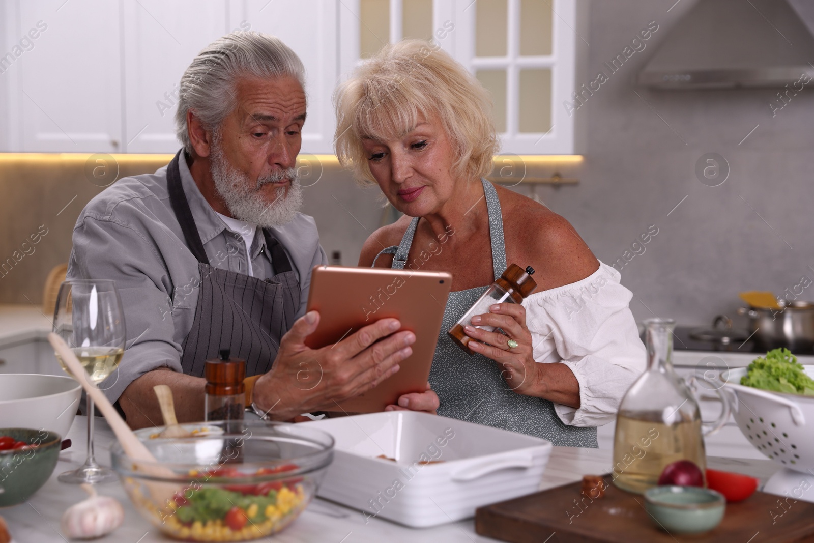 Elderly couple with tablet cooking together at table in kitchen Photo of Elderly couple with tablet cooking together at table in kitchen