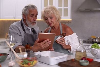 Photo of Elderly couple with tablet cooking together at table in kitchen