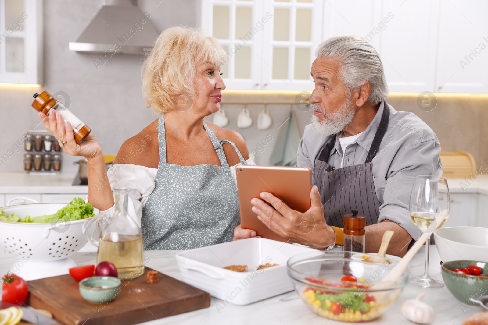 Elderly couple with tablet cooking together at table in kitchen Photo of Elderly couple with tablet cooking together at table in kitchen