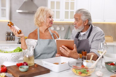 Photo of Elderly couple with tablet cooking together at table in kitchen