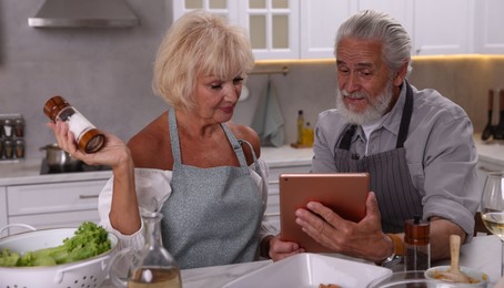 Photo of Elderly couple with tablet cooking together at table in kitchen
