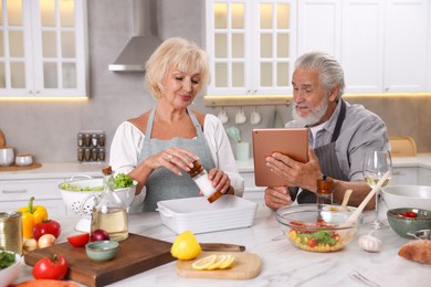 Photo of Elderly couple with tablet cooking together at marble table in kitchen