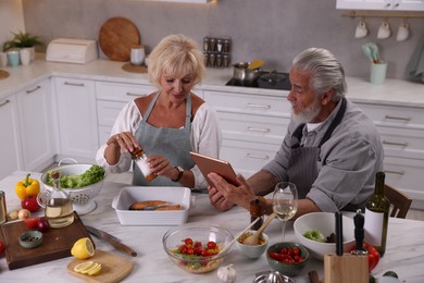 Photo of Elderly couple with tablet cooking together at marble table in kitchen