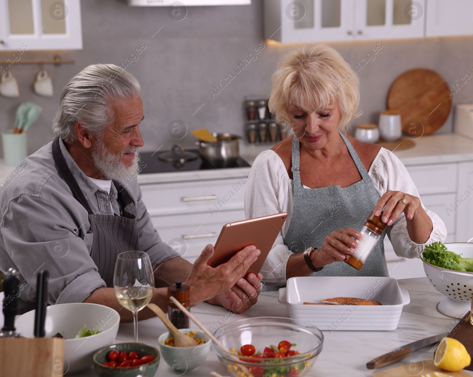Elderly couple with tablet cooking together at table in kitchen Photo of Elderly couple with tablet cooking together at table in kitchen