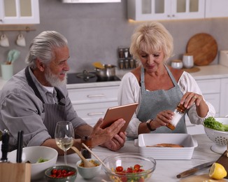 Photo of Elderly couple with tablet cooking together at table in kitchen