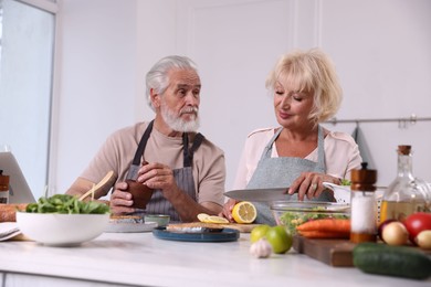 Photo of Elderly couple cooking together at table indoors