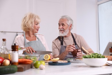 Photo of Elderly couple cooking together at table indoors