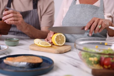 Photo of Elderly couple cooking together at white marble table indoors, closeup