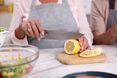 Photo of Elderly couple cooking together at white marble table indoors, closeup