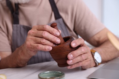 Photo of Elderly man with mortar and pestle at white marble table indoors, closeup