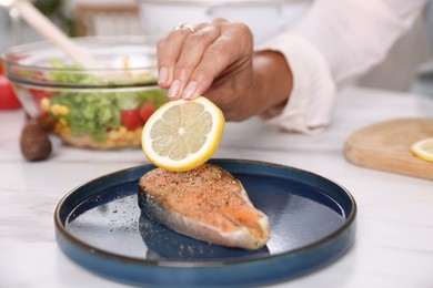 Photo of Senior woman putting slice of lemon onto salmon fish at white marble table indoors, closeup