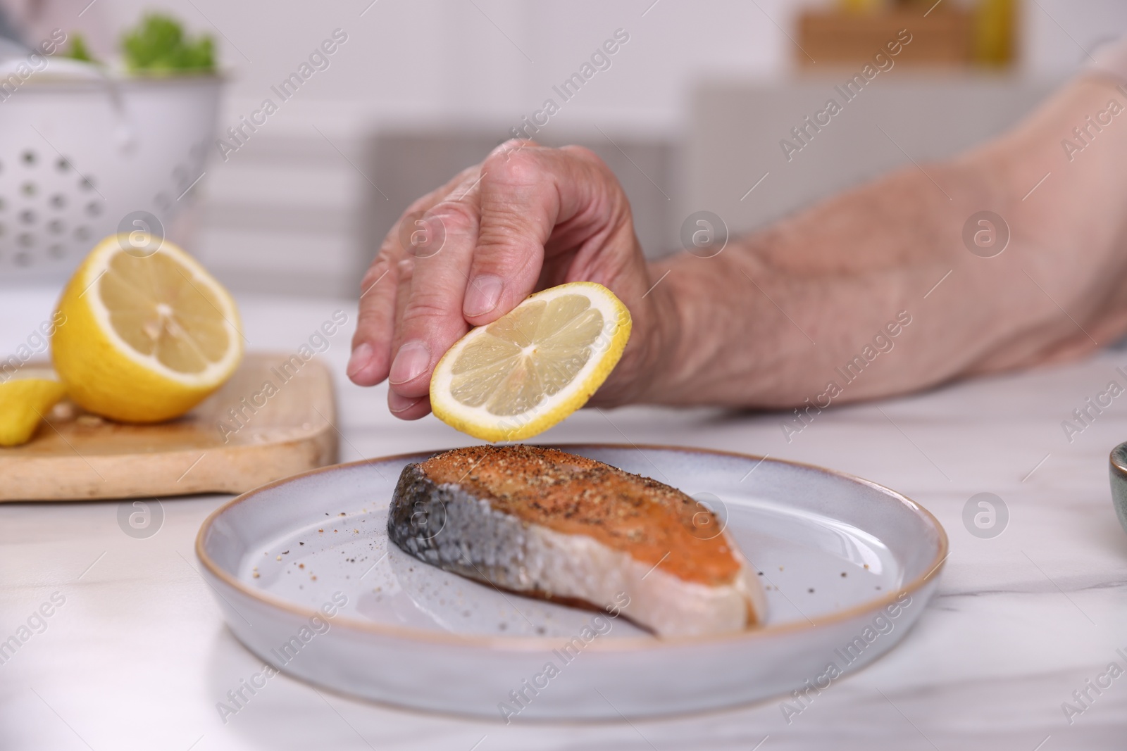 Elderly man putting slice of lemon onto salmon fish at white marble table indoors, closeup Photo of Elderly man putting slice of lemon onto salmon fish at white marble table indoors, closeup