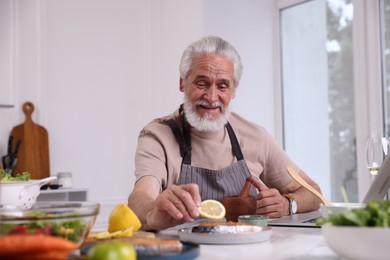 Photo of Elderly man putting slice of lemon onto salmon fish at white table indoors