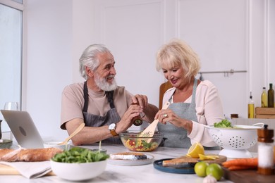 Photo of Elderly couple cooking together at table indoors