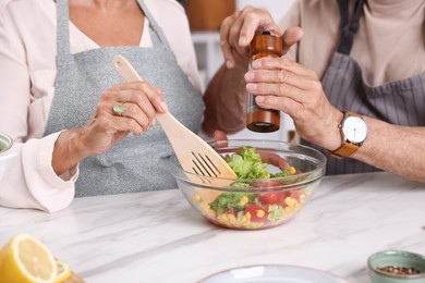 Photo of Elderly couple cooking together at white marble table indoors, closeup