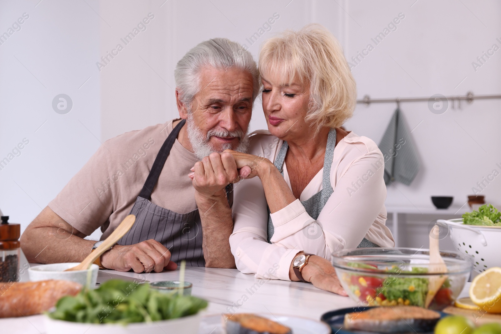 Elderly couple holding hands while cooking together at table indoors Photo of Elderly couple holding hands while cooking together at table indoors