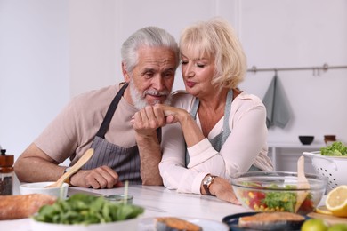 Photo of Elderly couple holding hands while cooking together at table indoors