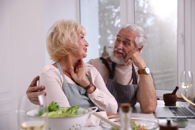 Photo of Elderly couple cooking together at table indoors