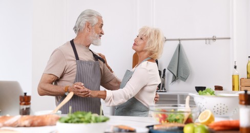 Photo of Elderly couple dancing after cooking together in kitchen