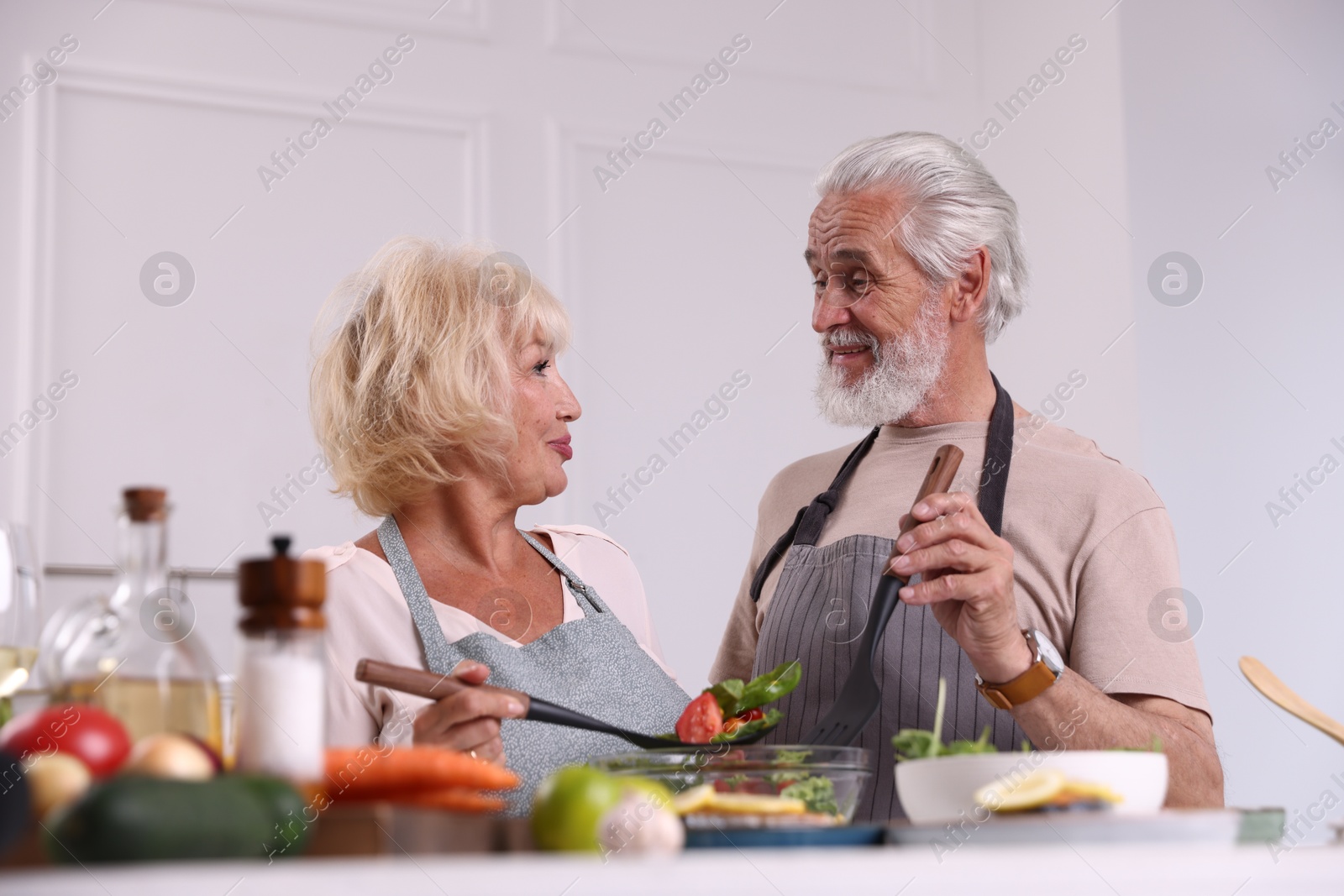 Elderly couple cooking together at table indoors Photo of Elderly couple cooking together at table indoors